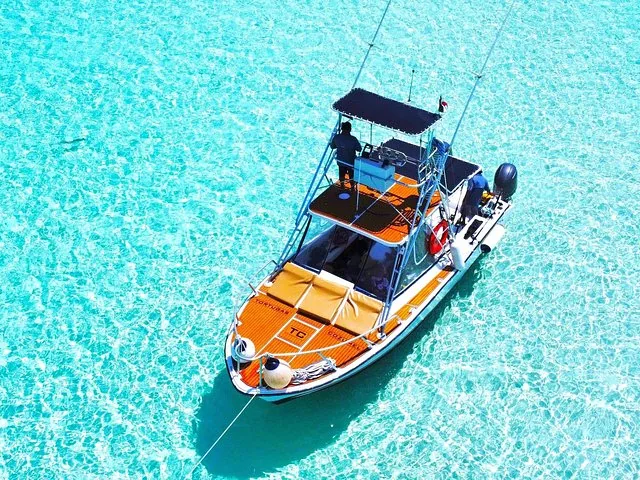 Draufsicht auf ein kleines Motorboot, das in kristallklarem türkisfarbenem Wasser vor Anker liegt.