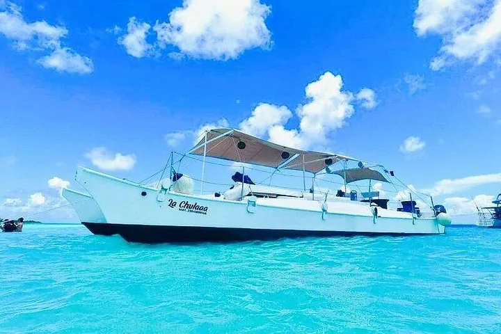 Ein weißer Katamaran namens „La Chulaaa“, der in leuchtend blauem Wasser vor Anker liegt.